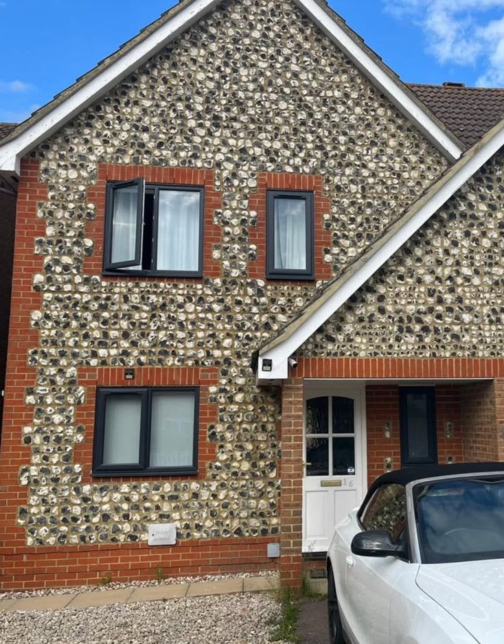 Flint-faced house with anthracite grey windows set in red brick surrounds