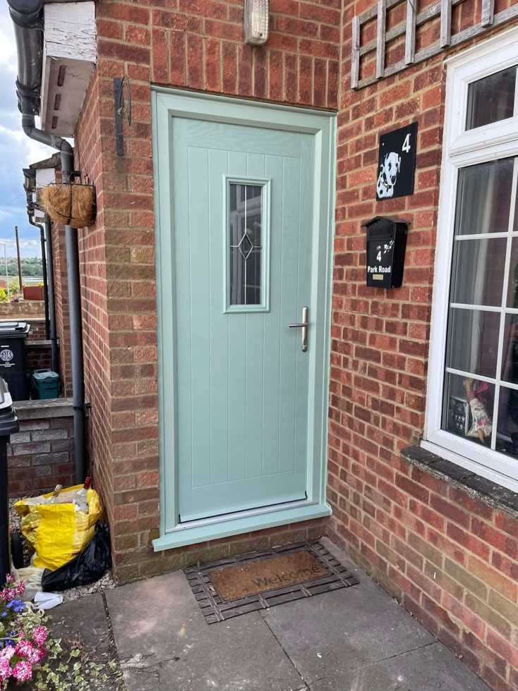 Pale green composite door with a glazed panel in a brick entrance