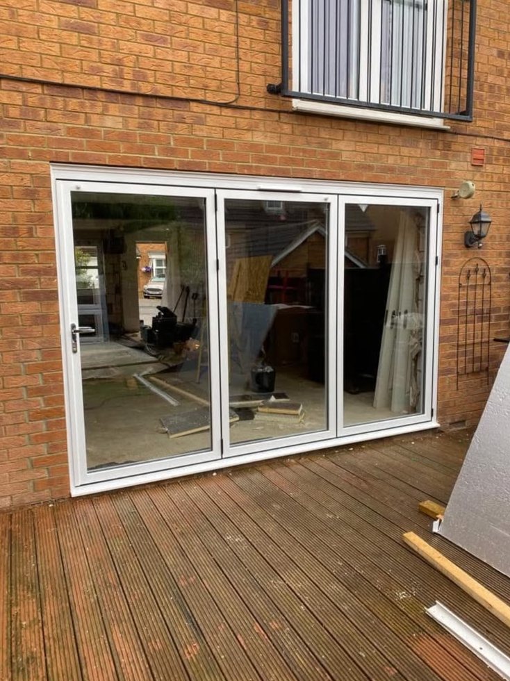 Three-panel white bifold doors fitted to the rear of a brick house